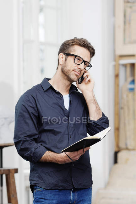 Businessman talking on phone while holding notebook — Stock Photo