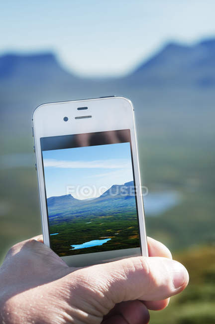Hand holding smartphone with photo of mountainous landscape — Stock Photo