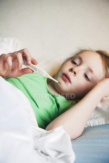 Дівчина лежить в ліжку з термометром — стокове фото