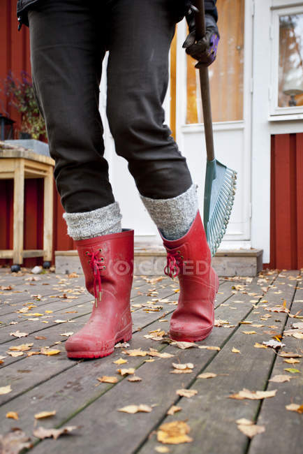 Cropped view of woman wearing rubber boots, holding rake — Stock Photo