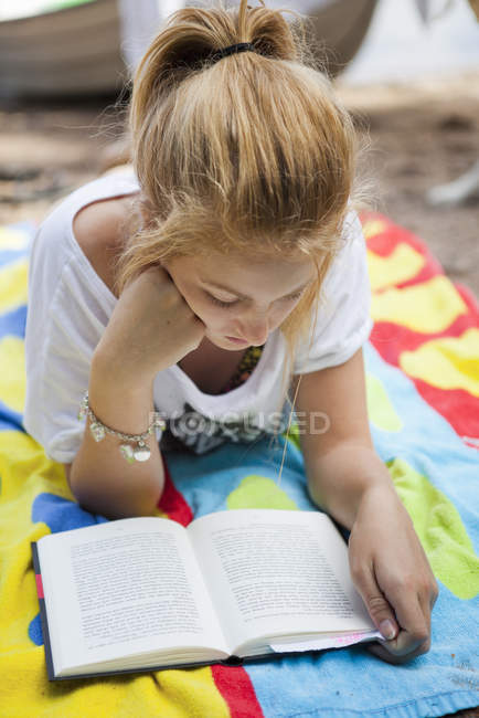 Дівчина-підліток лежить на пляжі і читає книгу — стокове фото