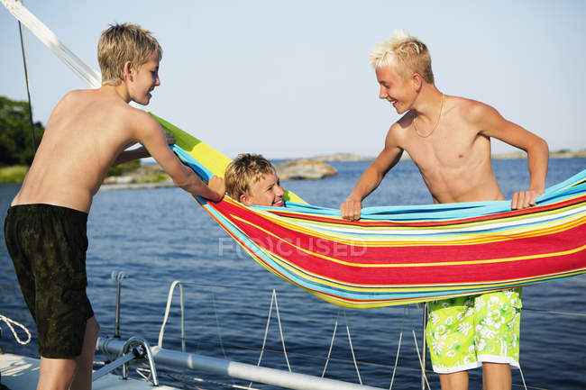 Три хлопчики-підлітки на човновій палубі і один хлопчик лежить в гамаку — стокове фото