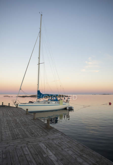 Sailboat in harbor by pier at evening — Stock Photo