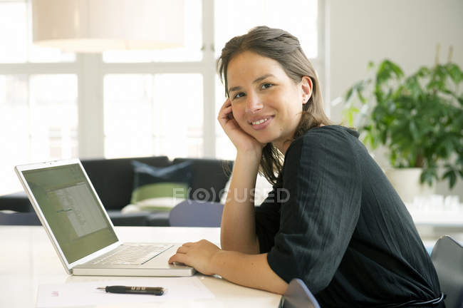 Porträt einer jungen Frau, die ihren Laptop benutzt und in die Kamera lächelt — Stockfoto