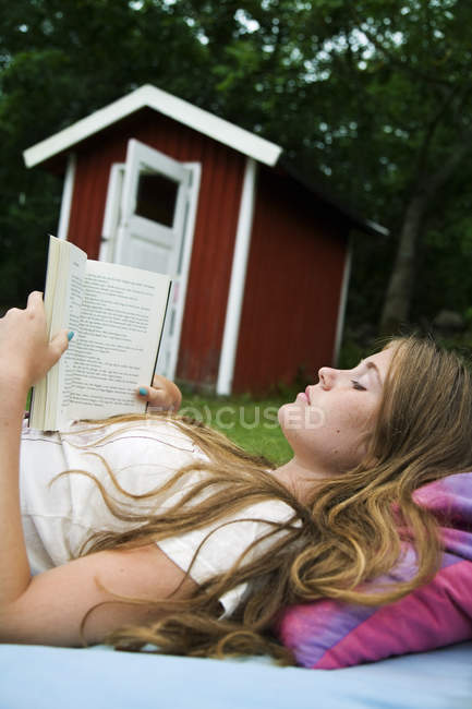 Mädchen liest Buch auf Liegestuhl im Garten — Stockfoto