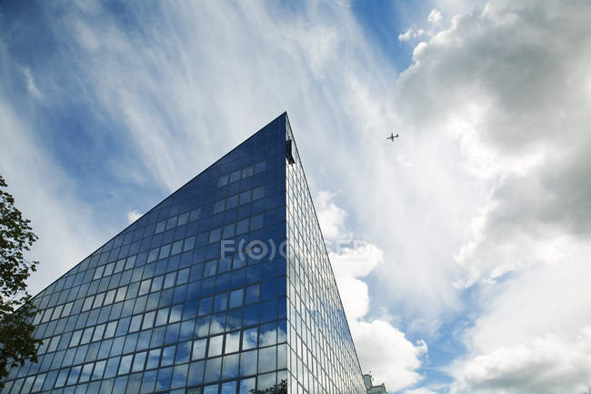 Façade de bâtiment moderne avec avion se déplaçant dans le ciel nuageux — Photo de stock