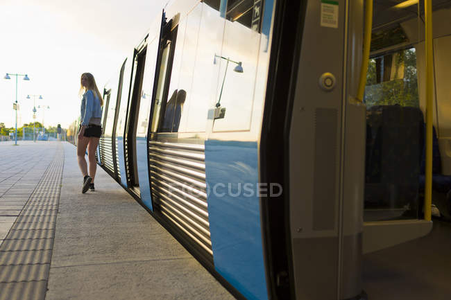 Adolescente caminhando ao longo do trem na plataforma da estação ferroviária — Fotografia de Stock