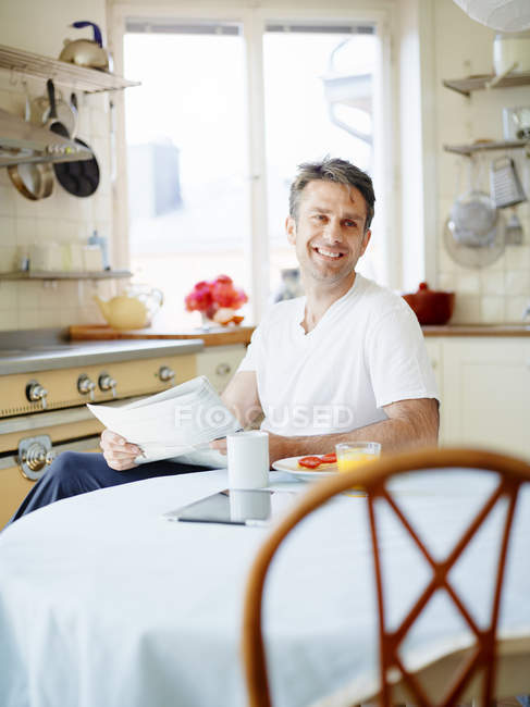 Man holding newspaper while sitting at breakfast table and smiling — Stock Photo