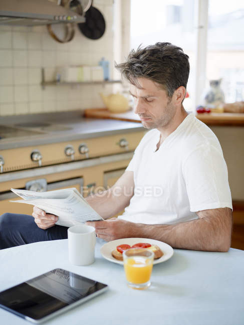 Man reading newspaper at breakfast table — Stock Photo