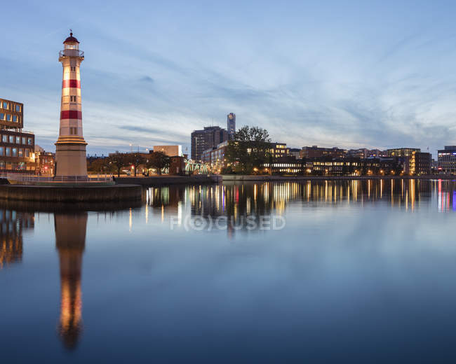 Lighthouse and cityscape at dusk, reflection at sea — Stock Photo
