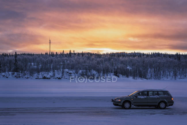 Carro em estrada de terra coberta de neve ao pôr do sol — Fotografia de Stock