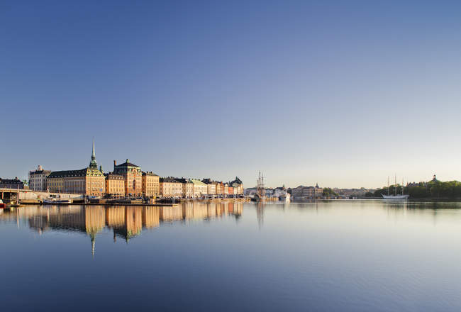 Edificios iluminados por el sol que reflejan en el agua del puerto, Estocolmo - foto de stock