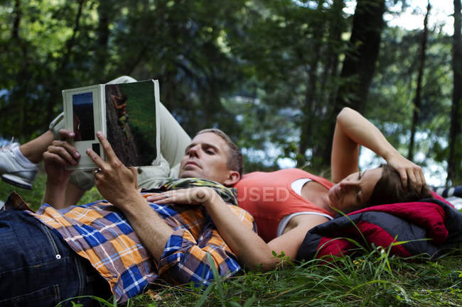 Randonneurs allongés sur l'herbe et le livre de lecture, se concentrer sur le premier plan — Photo de stock