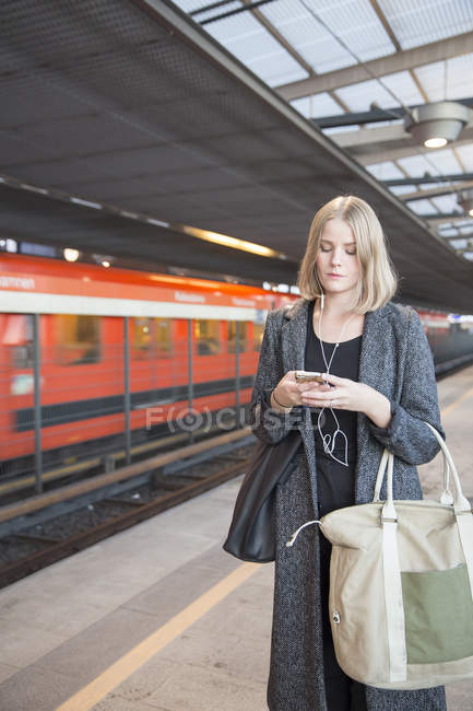 Jeune femme utilisant un smartphone sur la station de métro — Photo de stock