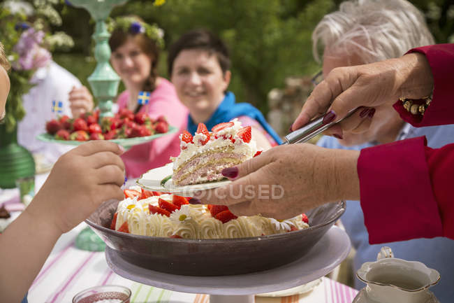 Vista recortada de la mujer poniendo rebanada de pastel en el plato para niña - foto de stock