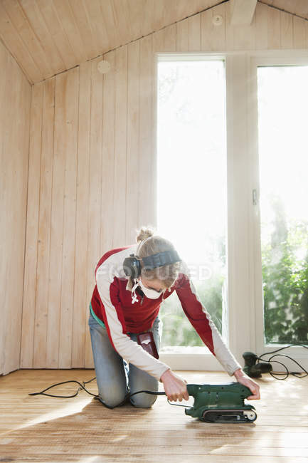 Woman in protective mask sanding hardwood floor — Stock Photo