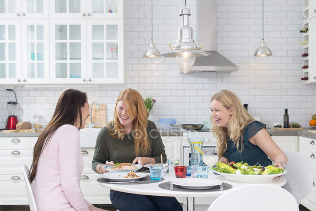 Drei lachende Frauen am Küchentisch — Stockfoto