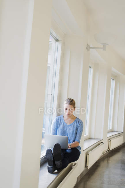 Junge Frau benutzt Laptop an der Universität auf Fensterbank — Stockfoto