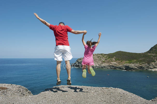 Задний вид отца, держащегося за руки с дочерью на скалистом пляже — стоковое фото