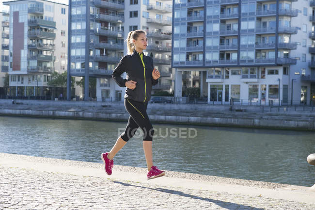 Woman with brown hair running along embankment — Stock Photo