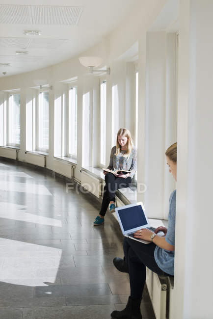 Junge Frauen lesen Buch und benutzen Laptop vor den Fenstern des Universitätsgebäudes — Stockfoto