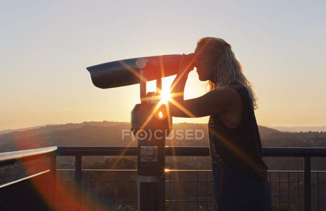 Woman using coin-operated binoculars at sunset in Los Angeles — Stock Photo