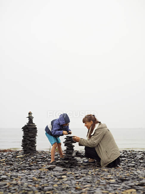 Madre e hija construyendo cairn en la playa - foto de stock