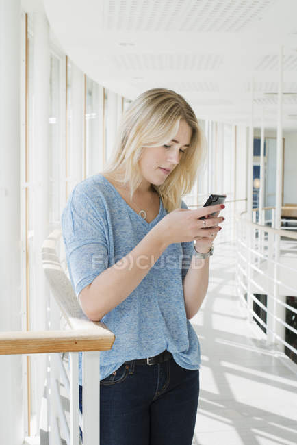 Молода жінка використовує смартфон у будівлі університету — стокове фото