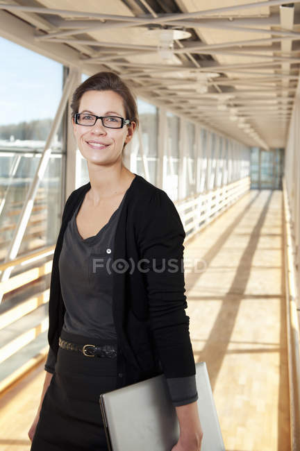Mujer de negocios con portátil de pie en el pasillo vacío - foto de stock