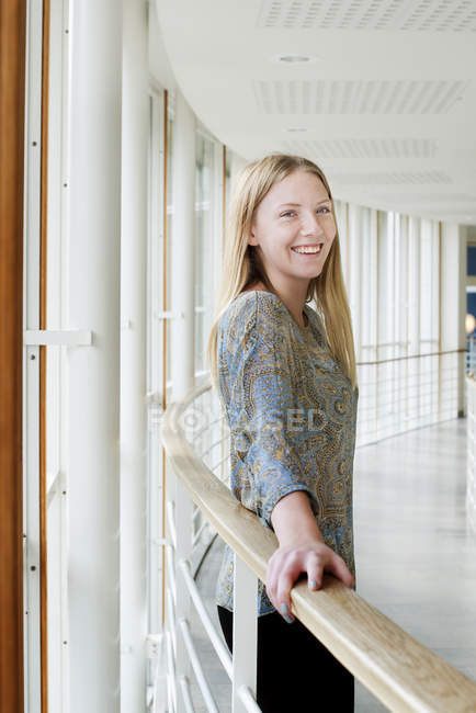 Retrato de estudante sorrindo inclinado na balaustrada dentro de casa — Fotografia de Stock