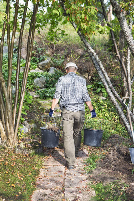 Rear view of man carrying buckets — Stock Photo