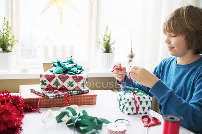Мальчик упаковывает рождественские подарки дома — стоковое фото