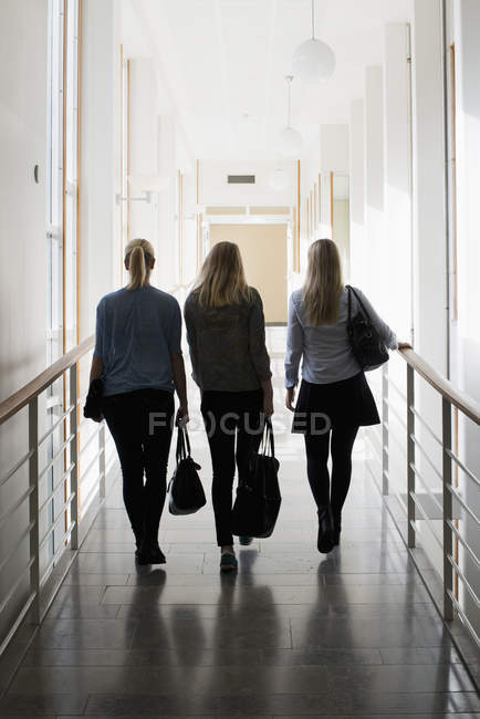 Visão traseira de estudantes do sexo feminino caminhando com sacos na universidade — Fotografia de Stock