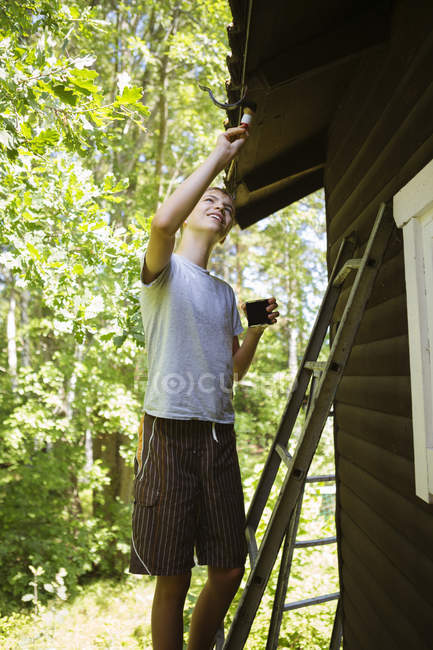 Teenage boy painting log cabin — Stock Photo