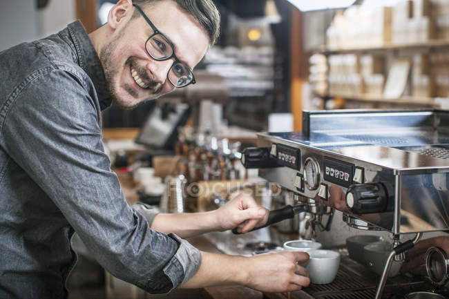 Barista sonriente haciendo café y mirando a la cámara - foto de stock
