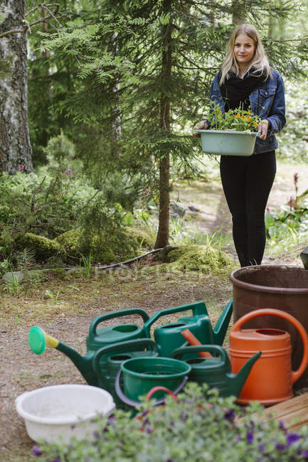 Young woman holding bowl with growing flowers in garden — Stock Photo