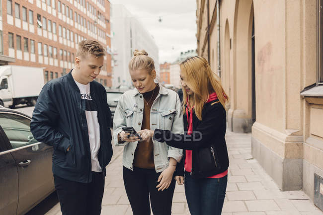 Подростки смотрят на сотовый телефон на улице, фокусируются на переднем плане — стоковое фото