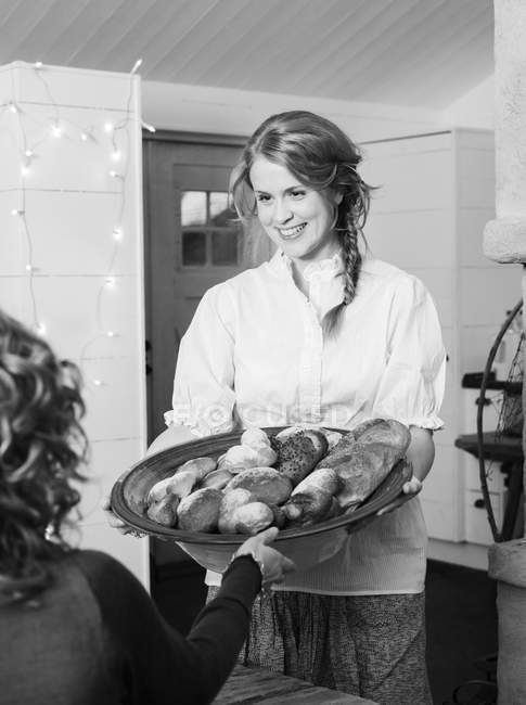 Young woman holding bread in serving dish, black and white — Stock Photo
