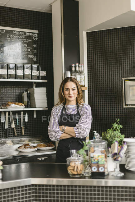 Portrait of barista with arms crossed behind counter in cafe — Stock Photo
