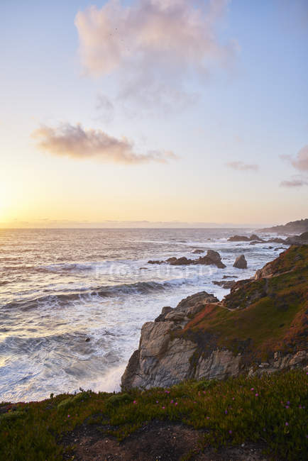Scenic view of waves by cliffs at sunset in Big Sur, USA — Stock Photo