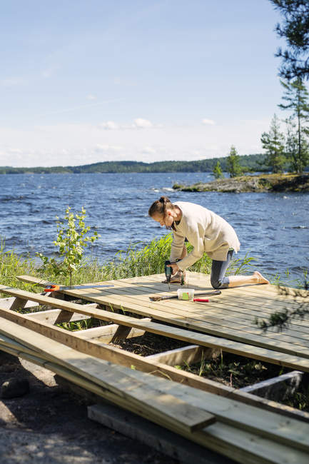 Convés de construção de mulher adulta média em frente ao lago na Finlândia — Fotografia de Stock