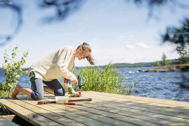 Средняя взрослая женщина строит палубу перед озером в Финляндии — стоковое фото