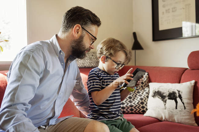 Padre y niño utilizando el dispositivo en la sala de estar - foto de stock