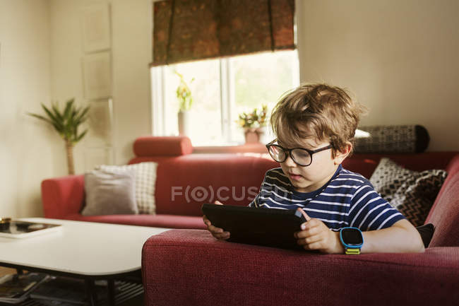 Хлопчик грає на цифровому планшеті у вітальні, фокус на передньому плані — стокове фото