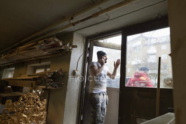 Homem adulto médio em pé na porta do negócio de carpintaria e falando no telefone celular — Fotografia de Stock
