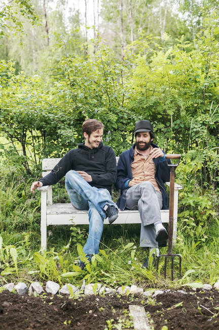 Amigos sentados con tenedor de jardinería al lado del jardín, enfoque selectivo - foto de stock