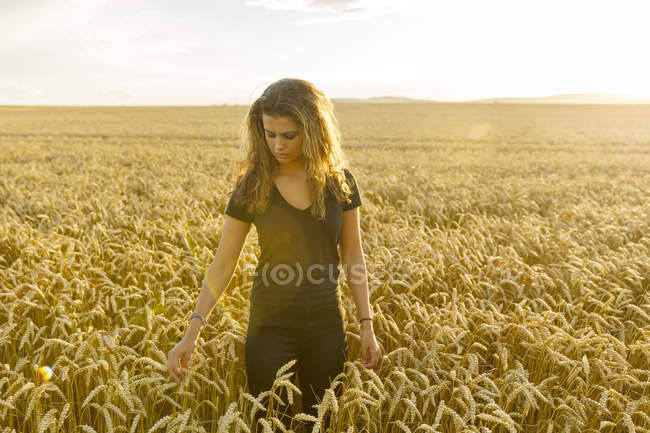 Девочка-подросток смотрит вниз на пшеничное поле, фокусируется на переднем плане — стоковое фото