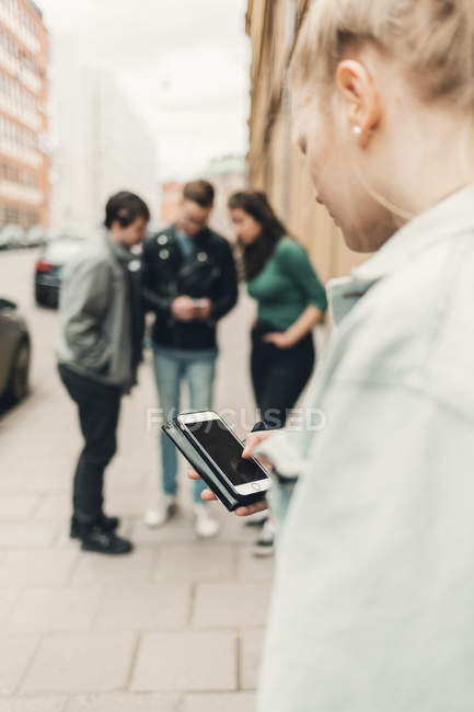 Chica adolescente comprobando el teléfono celular en la calle de la ciudad - foto de stock