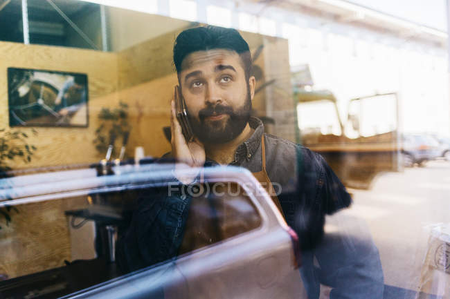 Coffee roaster talking on cell phone and looking through window — Stock Photo