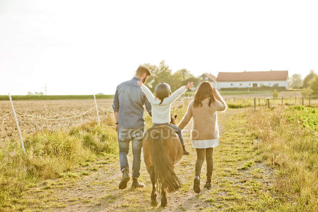 Visão traseira dos pais andando com a criança no cavalo — Fotografia de Stock